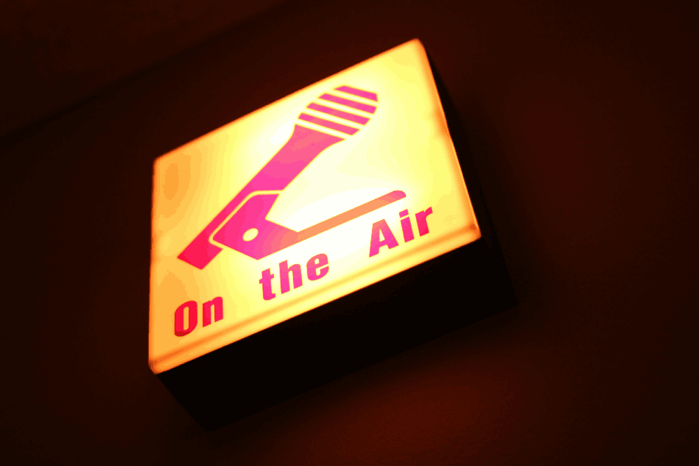 A sign with the words on the air showing a live podcast
